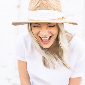 A beautiful woman with blond hair is laughing and wearing a sun hat with a ribbon.