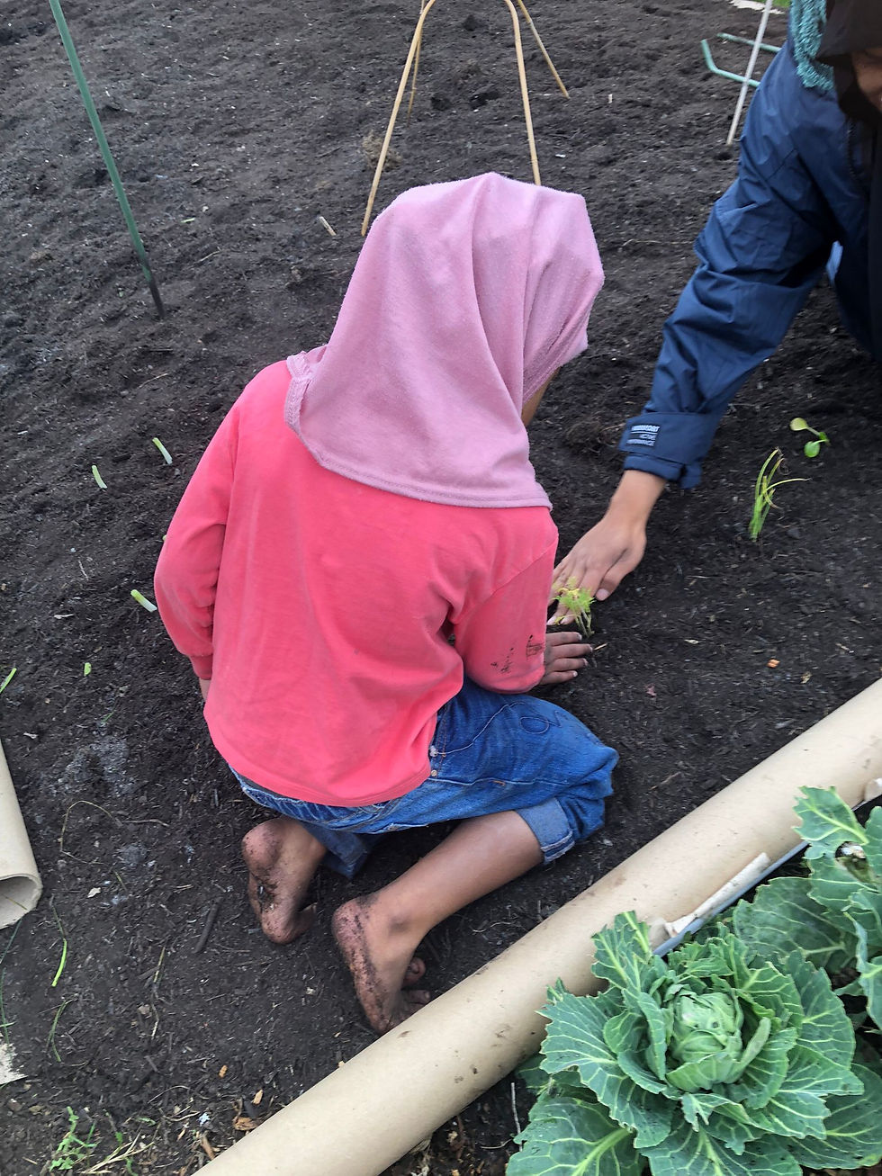 A child kneels barefoot on the rich soil, deeply engaged in planting alongside an adult, fostering a connection with the earth.