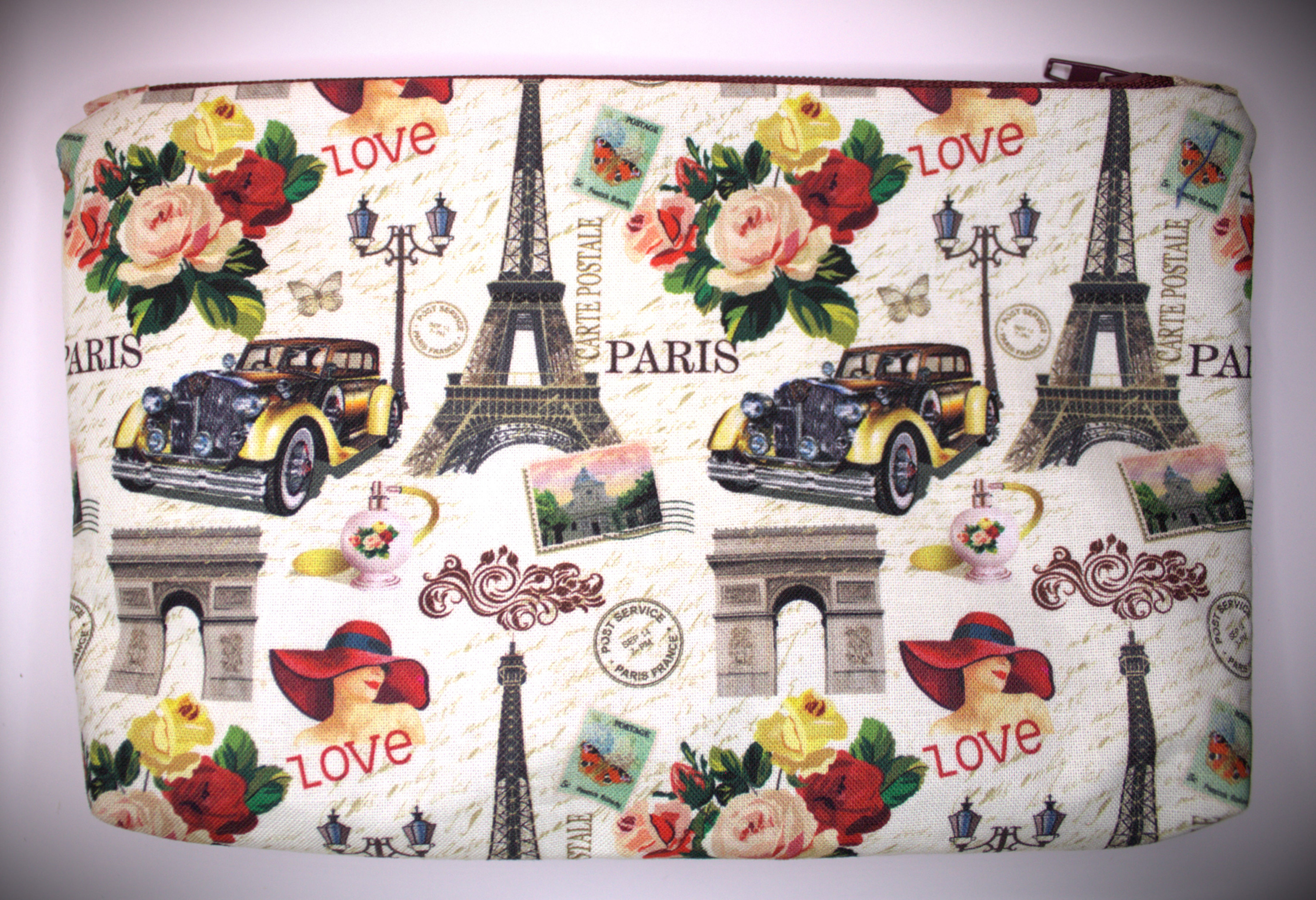 Zippered pouch approx. 8 inch wide by 6 inch. length, with wrist strap. White with Icons of France collaged pattern & the words Love Paris with bunches of flowers, matching maroon colored zipper.