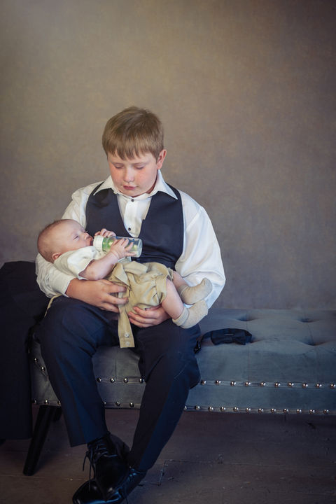 Young boy in vest feeding baby a bottle at a wedding