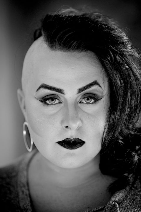 Black and white headshot of person with shaved hair, dark makeup.