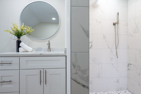 Bathroom with white vanity, round mirror, and tiled shower