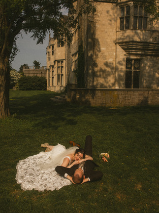 A bride and groom laying together on the grass in front of a stone castle at Planting Fields Arboretum