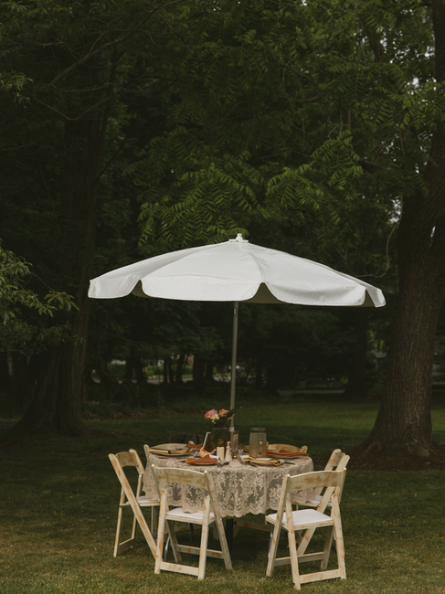 A wedding reception setup for a backyard wedding with an umbrella-covered table with a lace tablecloth