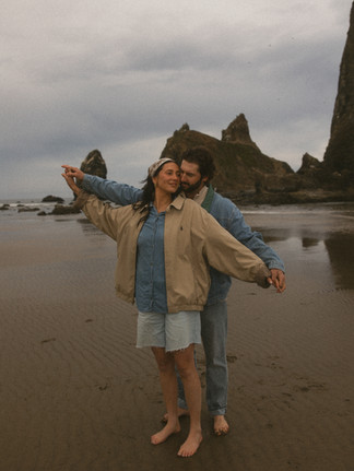 A couple wearing all denim outfits for a beach photoshoot, both holding out their arms