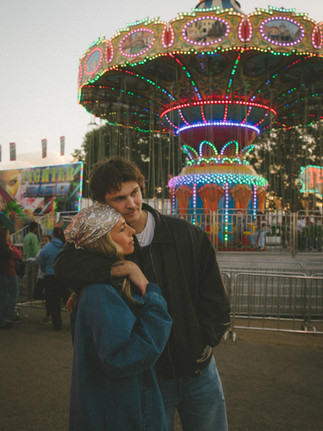 A couple hugging in front of fair rides