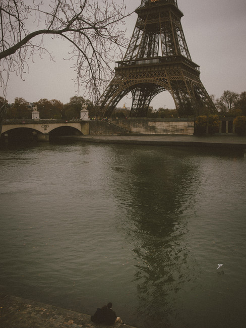 A couple sitting in front of the Seine with the Eiffel Tower in the background