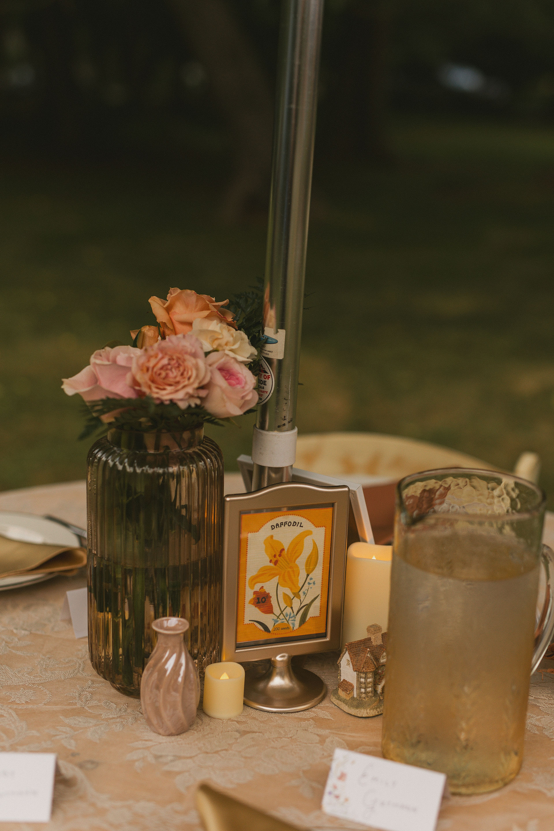 A wedding reception table setup at a backyard wedding with a pitcher, flowers, and table numbers