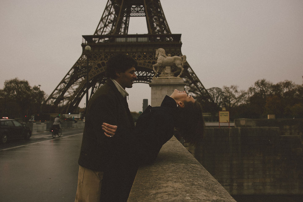 A girl leaning her head back while her husband smiles at her in front of the Eiffel Tower