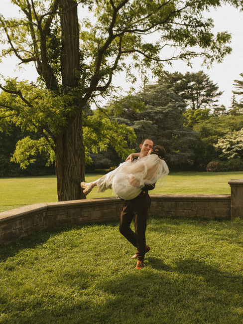 Groom holidng bride and spinning her in a field at planting fields arboretum