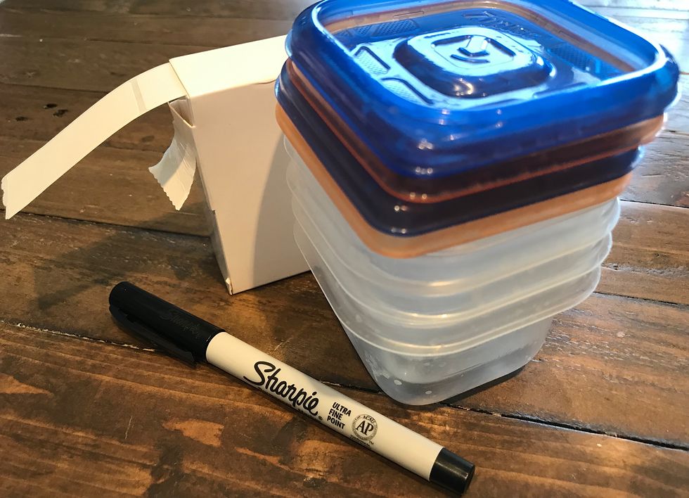 Image shows a stack of small plastic storage containers with blue and orange lids, a box containing a reel of white adhesive labels, and a Sharpie pen on a wooden table