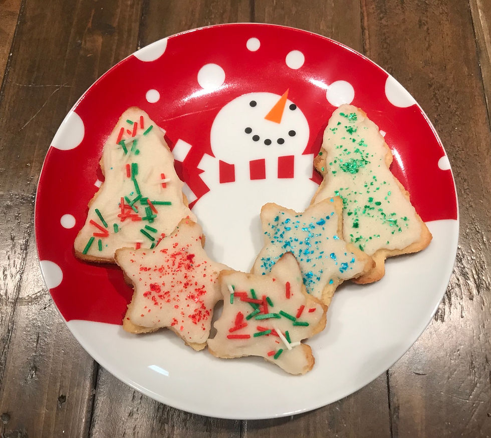 Image shows five decorated sugar cookies on a ceramic plate showing a white snowman on a field of snow and a red background with falling circles of snow. The cookies are Christmas tree and star shaped with white icing and a variety of colors of sprinkles decorating them.