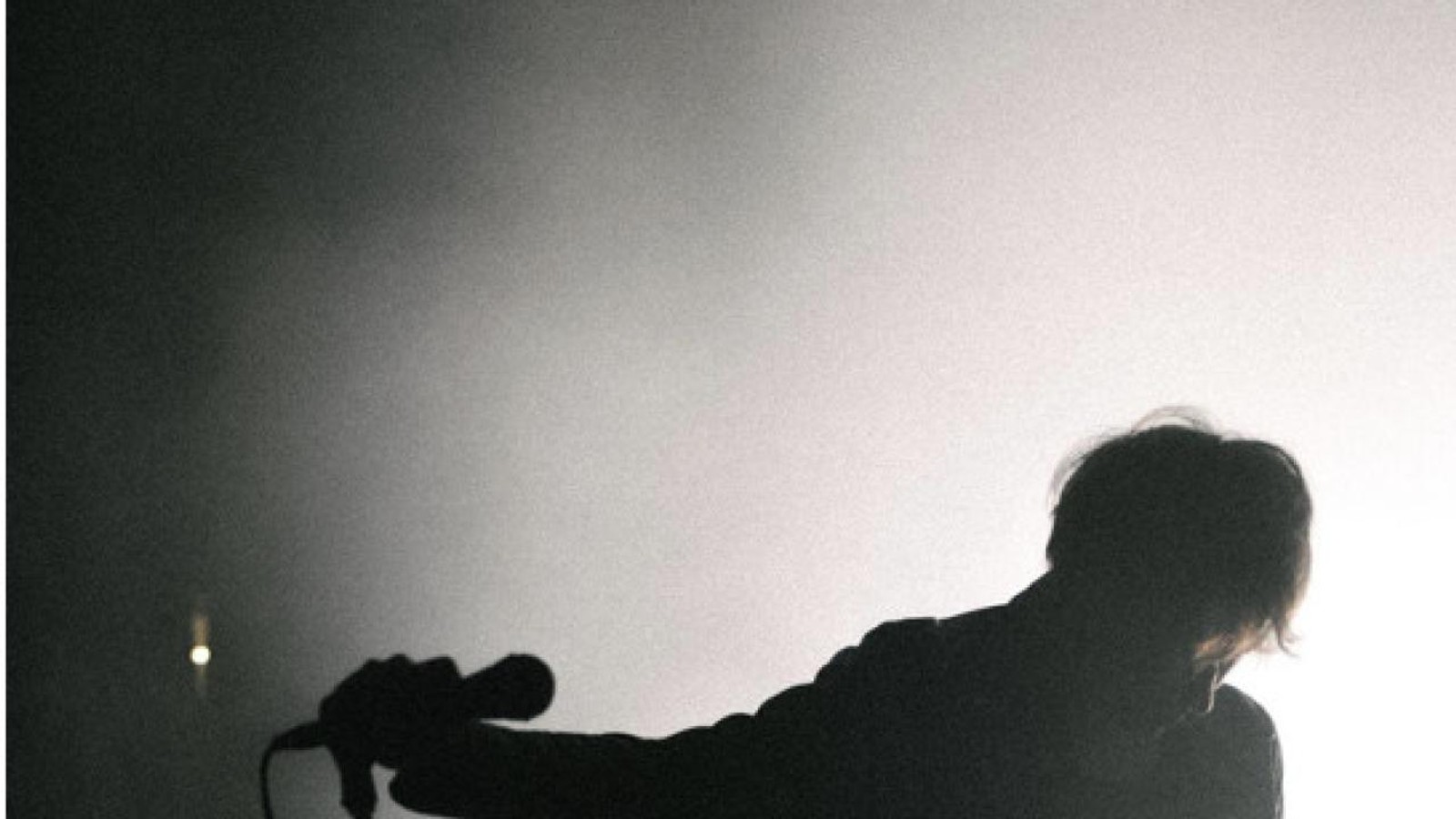 A member of The Howlers silhouetted beside a microphone in a monochrome promotional photograph for the album Heavy