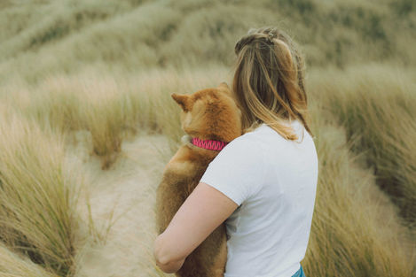 Vrouw knuffelt hond in duinen.