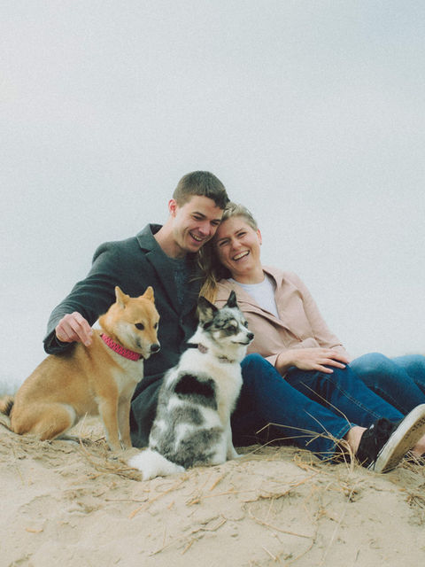 Man en vrouw zitten met twee honden op het zand