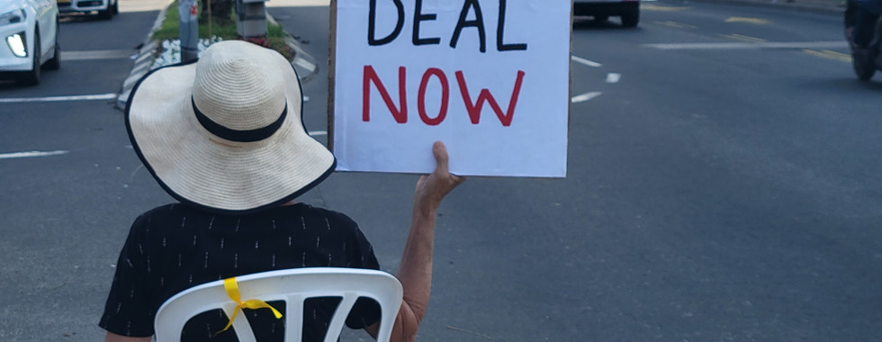 מפגינה יושבת עם שלט באנגלית prisoner deal now