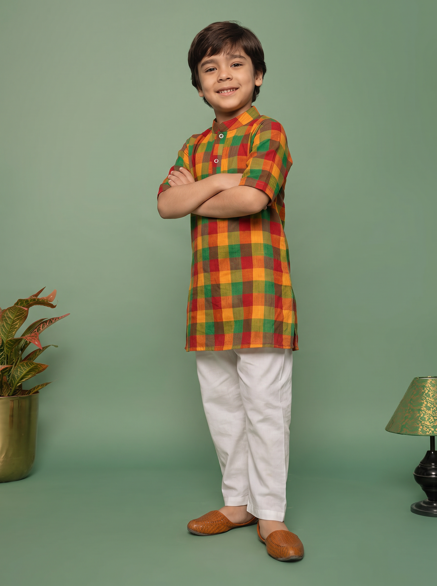 Boy standing in a multicolour check kurta and white pant against a sage green wall