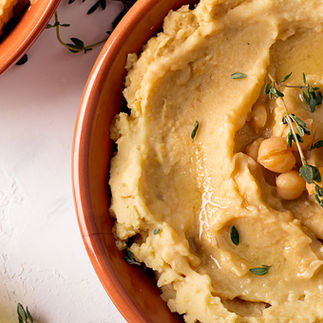 Close-up of creamy hummus with chickpeas and herbs in a terracotta bowl.