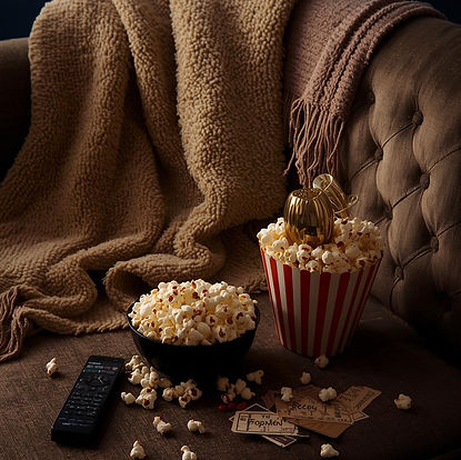 “Cozy movie night scene with gourmet popcorn in a bowl and striped popcorn tub on a sofa, surrounded by a soft blanket, remote control, and movie tickets, creating a warm, cinematic at-home experience.”