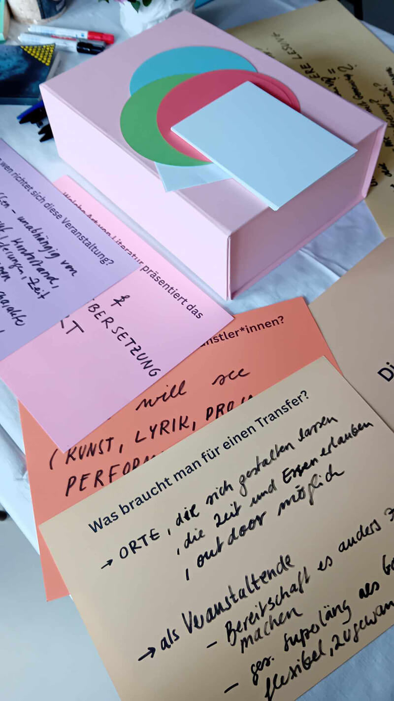 Closeup des Tisches (rosa Box, Stifte, bunte Blätter, mit Handschrift beschrieben).