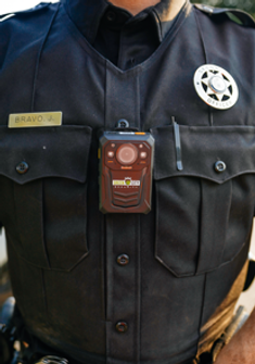 zoomed in on the chest of a uniformed guard, wearing the insignia of Green City Security, a metal tag with his name: Bravo J. on it and in the center a small square black device that is used to record and communicate