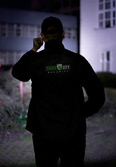 A security officer with his back turned shining a flashlight into a dark neighborhood