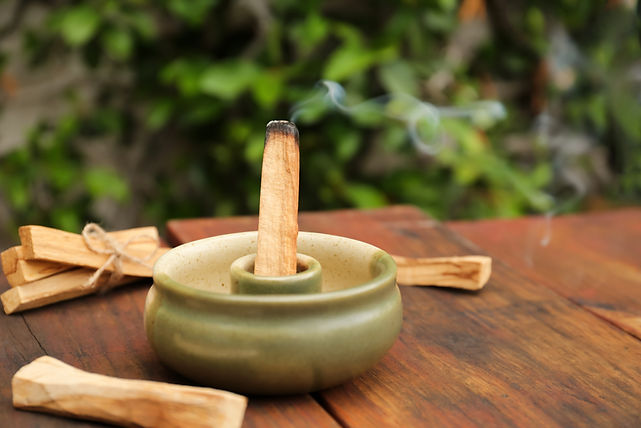 Palo Santo stick smoldering in holder on wooden table outdoors.jpg