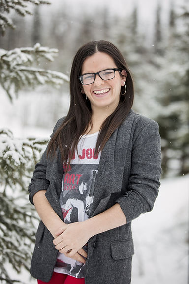 Katie stands in a snowy forest smiling.