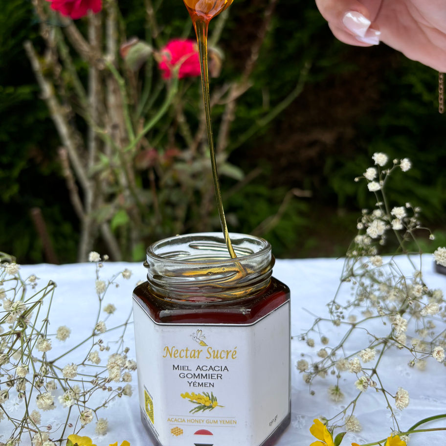 Pot de Miel d’acacia gommier du Yémen Nectar Sucré, coulant d’une cuillère en bois au-dessus du pot ouvert.