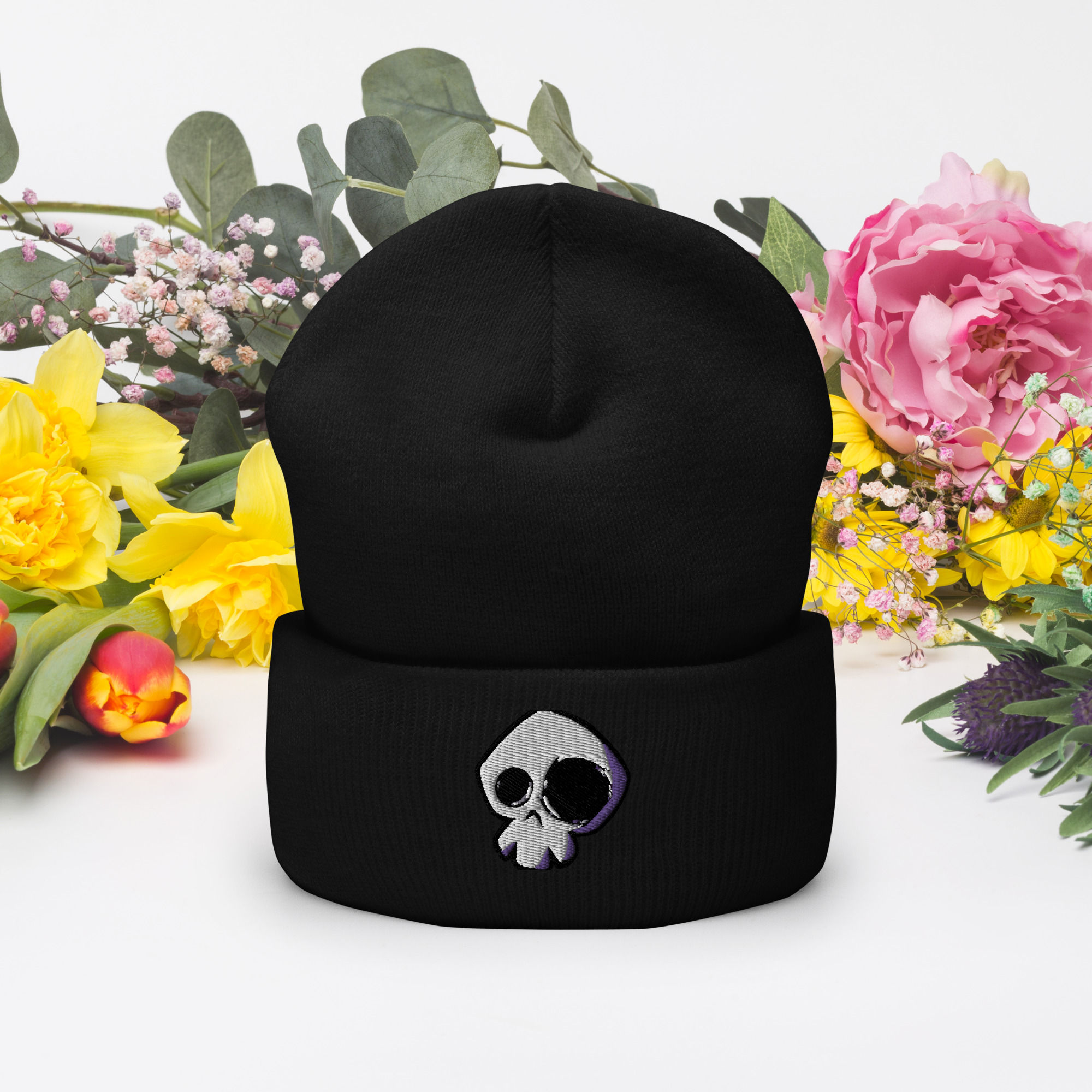Black beanie with skull design against floral background. www.r1clothing.com