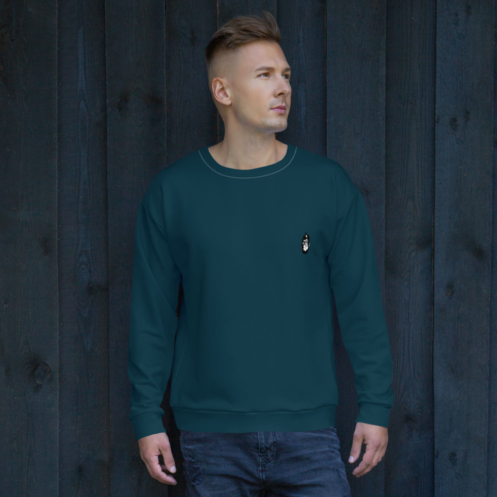 Man wearing teal sweatshirt with small logo on a dark wooden background.