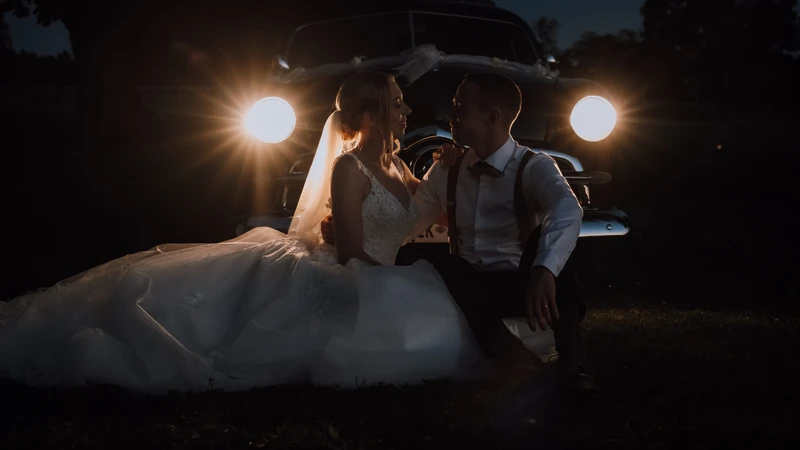 Brudpar sitter framför en veteranbil i mörkret, upplysta av bilens strålkastare. Dokumentär bröllopsfotografering med fokus på känsla, närvaro och äkta ögonblick.