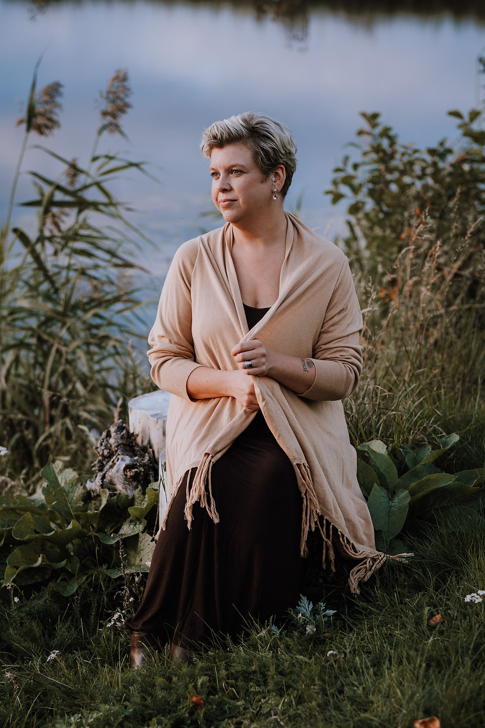Porträtt av kvinna som sveper en kofta om sig sittandes på en sten med sjön bakom sig