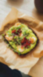 A slice of toasted bread topped with avocado spread, shrimp, sun-dried tomatoes, and microgreens.