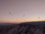 Hot air balloons ascend against a pastel sky at sunrise, casting silhouettes over a mountainous landscape in the Atlas Mountains, Morocco.