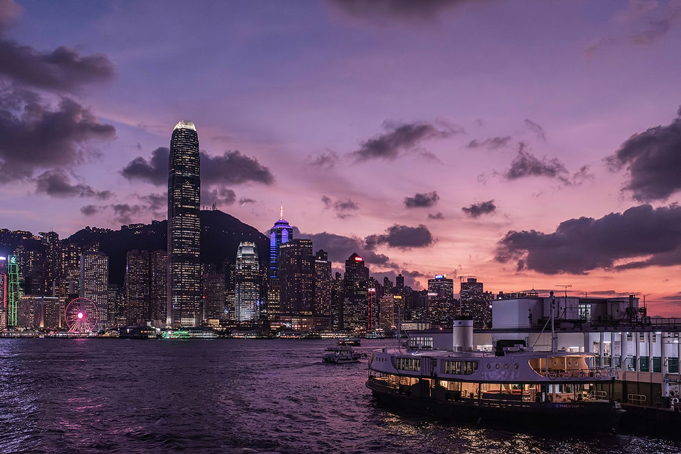 A city skyline silhouetted against a sunset, with clouds in the sky and reflections on the water. A ferry navigates through the lake or river in the foreground, surrounded by towering skyscrapers and urban buildings. The scene captures a tranquil moment as dusk falls over the metropolis.