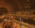 A bustling shopping mall adorned with festive lights and Christmas trees, featuring a spacious, arching glass ceiling.