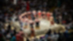 Many sumo wrestlers in a ring, with a large crowd watching. Some wrestlers are facing away while others stand in different poses. 