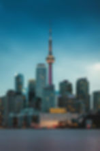 The iconic CN Tower illuminated at dusk, surrounded by Toronto's skyline, reflecting in the calm waters below.