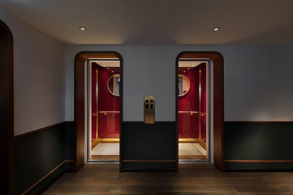 Dimly lit hallway with two open elevator doors, featuring elegant red interiors with circular mirrors. Wooden paneling adds warmth and sophistication.