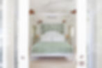 Bright, airy bedroom featuring a four-poster bed with green botanical-patterned linens and soft white bedding, illuminated by natural light.