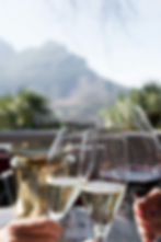 Three glasses of champagne and red wine clinking together, with mountains in the background.