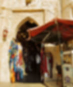 A colourful display of clothing hangs outside a market entrance with an arched doorway.
