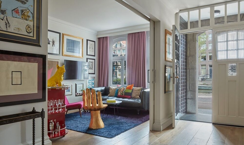 A stylish interior featuring a cozy living room with art, a blue rug, and an open doorway revealing a canal view outside.