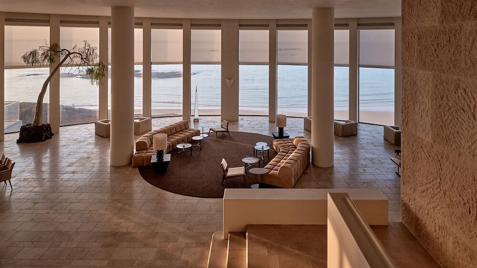Modern beachfront lounge with elegant furniture, large windows, and serene ocean views at sunrise, featuring a minimalist decor.