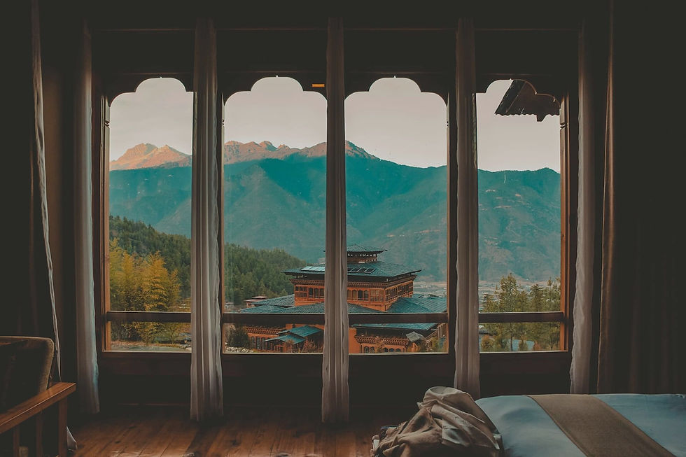 A cozy room featuring a large window that offers a scenic view of mountains and trees. The interior includes stylish furniture, with wooden flooring and decorated walls, creating a warm and inviting atmosphere.