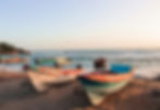 Colourful fishing boats on a sandy beach, with ocean waves in the background. 