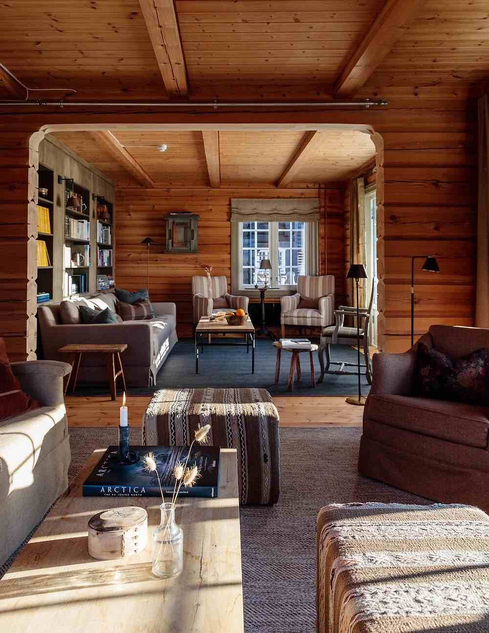 Cozy wooden living room with two striped chairs, a coffee table, bookshelves, and warm lighting, creating a welcoming atmosphere.