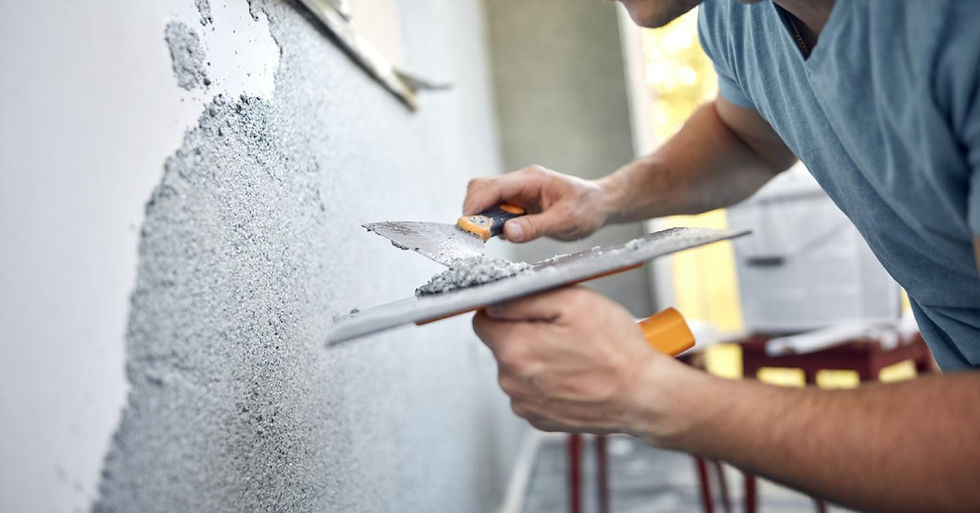 A person working on a home repair, as they smoothing out stucco on the half-finished wall in front of them.