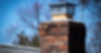 A metal chimney cap installed on top of a chimney. The brick chimney is on a gray rooftop.